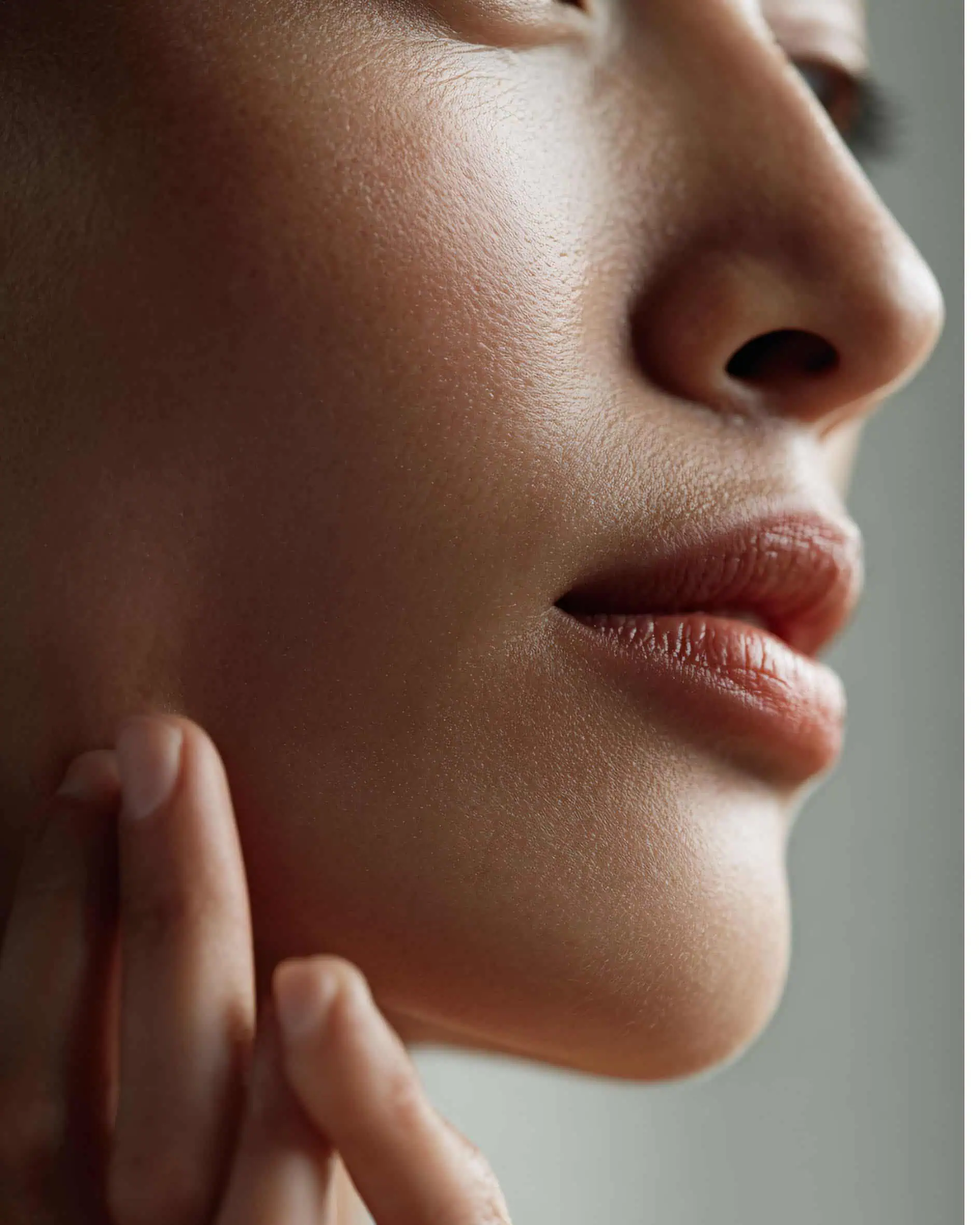jawline Gros plan du bas d’un visage montrant joue, nez, lèvres légèrement entrouvertes et menton, avec des doigts effleurant la mâchoire et une peau lisse et texturée.