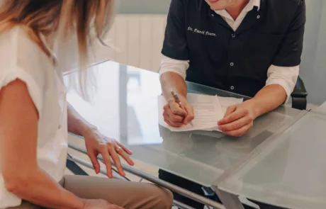 clinique des musicnes à Nice 8 Patiente assise en face d'un médecin à un bureau en verre pendant que le médecin écrit et signe des documents posés entre eux.